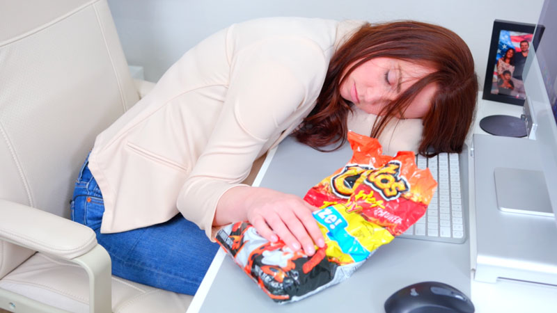 Woman asleep at desk clutching Flamin' Hot Cheetos bag